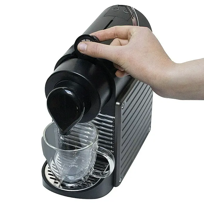 Cápsulas de café reutilizables - 3 ud., Específico para: Nespresso - Una máquina de café de cápsulas negra dispensa café en una taza transparente mientras una mano opera el mecanismo.