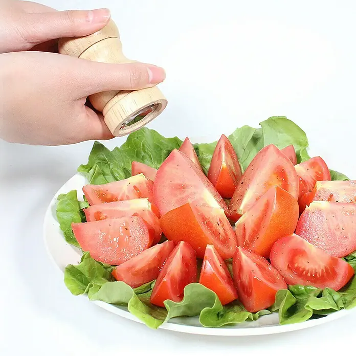 Molinillo de sal y pimienta - 4,9 mm x 10 cm, 25 ml - Un plato de tomates y lechuga está siendo sazonado con un molinillo de especias de madera, mejorando el sabor.
