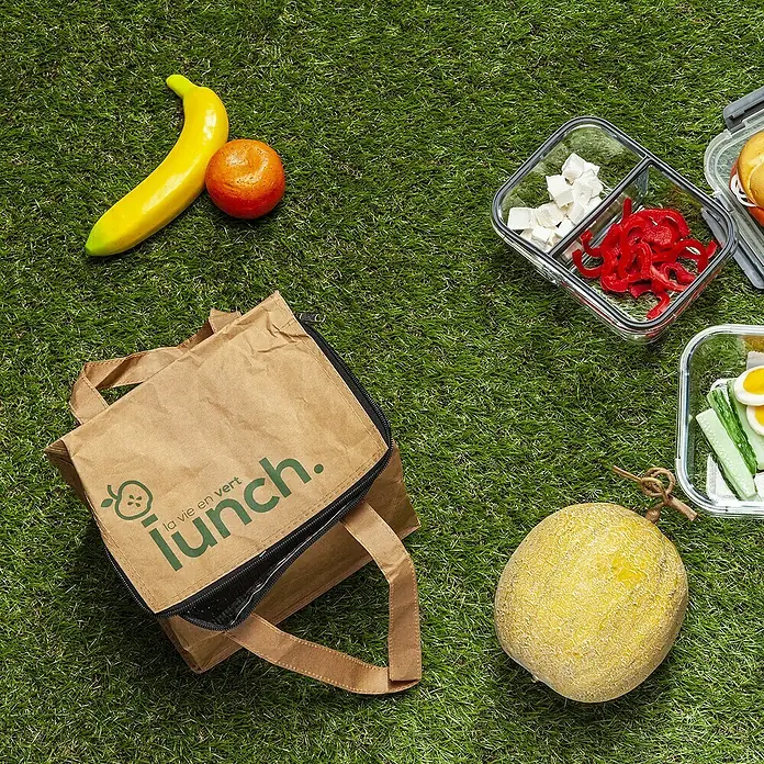 Bolsa isotérmica - L x An x Al: 17,5 x 22 x 16 cm, Beige - Bolsa nevera marrón "La vie en vert lunch." con recipientes reutilizables y fruta sobre hierba verde.