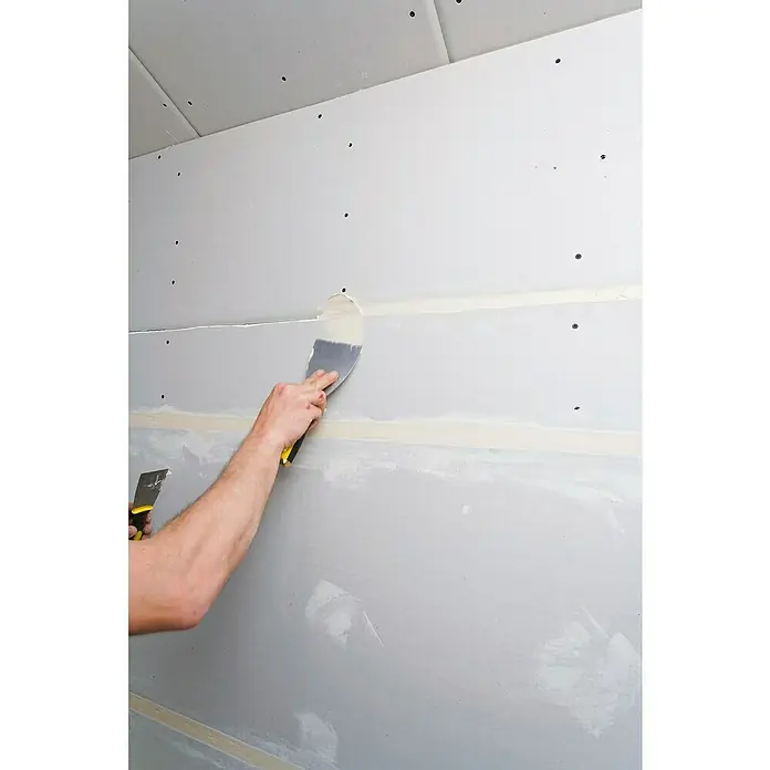 Knauf Feinspachtel Uniflott Finish - 4 kg, Gebrauchsfertig - Ein Arbeiter spachtelt eine Gipskartonwand mit einem Spachtel, um Unebenheiten auszugleichen und eine glatte Oberfläche zu erzielen.