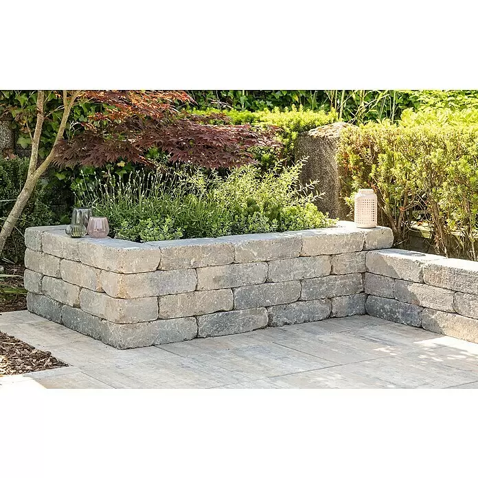 Diephaus Mauerstein Austin - 30 x 20 x 10 cm, Muschelkalk, Beton - Erhöhtes Blumenbeet aus grauen Betonsteinen mit Pflanzen, das eine Terrasse begrenzt.