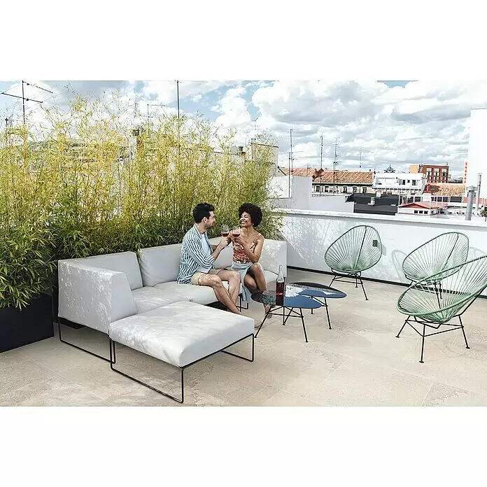 Terrassenfliese Jura 2.0 - 60 x 60 x 2 cm, Beige, Matt - Ein Paar entspannt auf einem modernen weißen Outdoor-Sofa und stößt mit Rotweingläsern auf einer Dachterrasse mit grünen Drahtstühlen an.