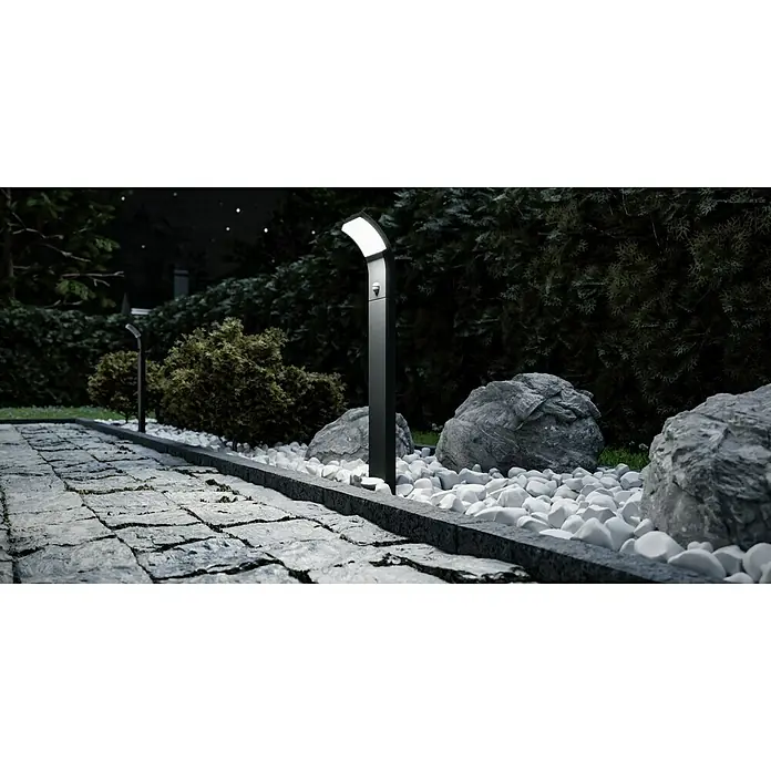 Starlux LED-Außenwegleuchte Udine7 W, Warmweiß, Höhe: 600 mm, IP54 - Das Bild zeigt eine moderne Außenleuchte, die einen Gartenweg beleuchtet, umgeben von Steinen und üppigem Grün.