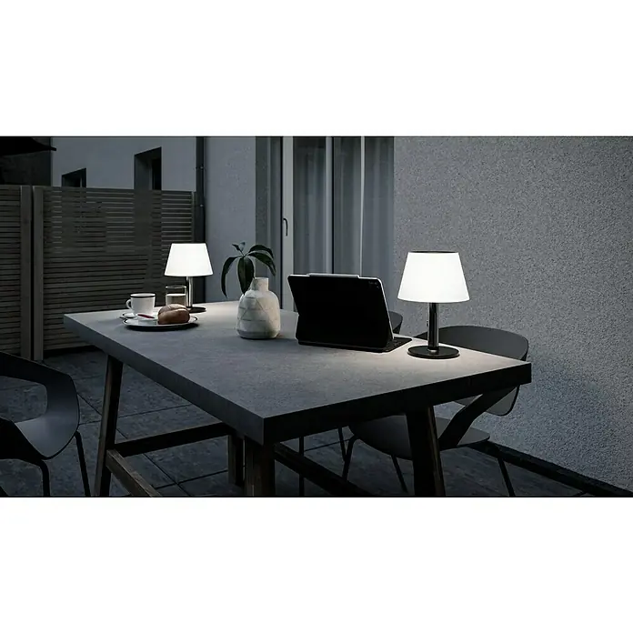 Paulmann Solar-Dekoleuchte Lillesol - 0,8 W, Edelstahl, IP44 - Eine stimmungsvolle Szene mit zwei Tischlampen, einem Tablet und Geschirr auf einem grauen Tisch im Außenbereich.