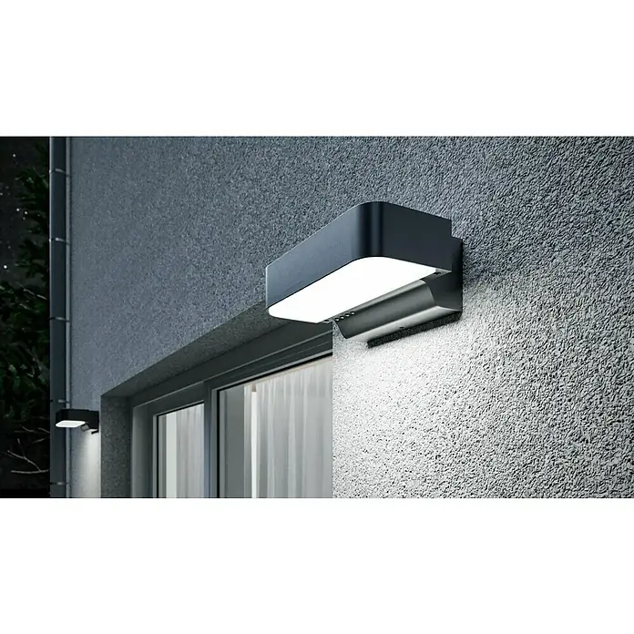 Steinel Aplique exterior LED con sensor L 800 SC - L x An x Al: 14,6 x 23 x 8,8 cm - Una lámpara de exterior gris moderna está montada en una pared texturizada, iluminando el área debajo con una luz brillante.