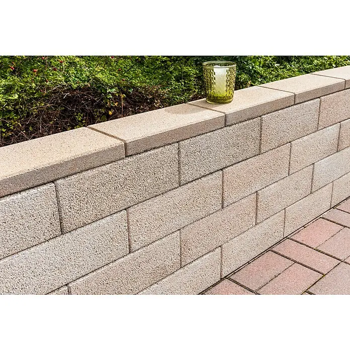 Diephaus Mauerstein Logan - 45 x 22,5 x 16,5 cm, Sandstein, Beton - Nahaufnahme einer beigen Steinmauer im Freien, gekrönt von einem dekorativen gelben Glas, das einen Hauch von Eleganz verleiht.