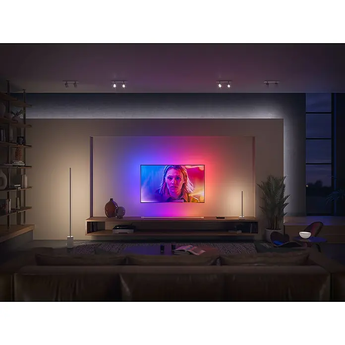Philips Hue LED-Band Ambiance Gradient Erweiterung - Länge: 1 m, RGBW - Ein modernes Wohnzimmer mit einem Philips Ambilight Fernseher, der die Wand farbig beleuchtet, und zwei Stehlampen.