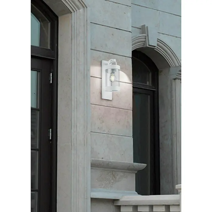 Trio Lighting Aplique exterior Sambesi - 28 W, L x An x Al: 12 x 12 x 33 cm, Blanco, E27 - Primer plano de una lámpara de pared exterior blanca con una pantalla transparente, que emite una luz cálida e ilumina la fachada elegantemente.