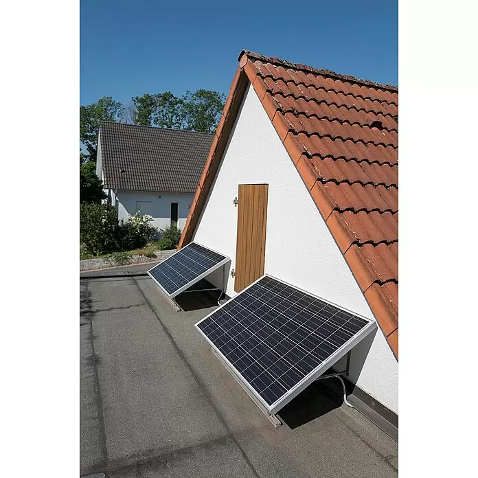 Sunset Balkonkraftwerk SunPay 600W inkl. Halterung - 0% MwSt. (gem. § 12 Abs. 3 UStG) - Monofazial, 600 W, L x B x H: 3,5 x 99,2 x 148 cm - Zwei schwarze Solarpaneele auf einem Flachdach neben einer weißen Wand mit rotem Ziegeldach.