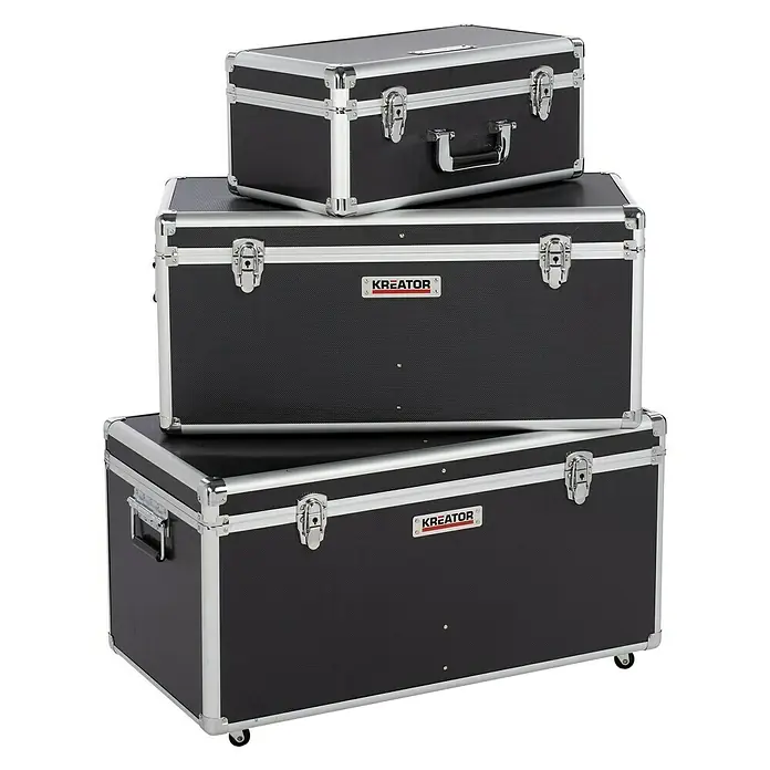 Kreator Juego de cajas de herramientas KRT640501B - 3 pzs., Ruedas, Con cerradura - Pila de tres maletas de aluminio negro Kreator con herrajes y asas plateadas sobre un fondo negro.