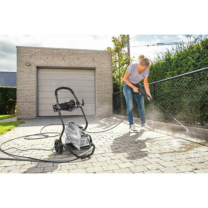 PowerPlus Hidrolimpiadora de alta presión POWXG90430 - 190 bar, 3.100 W, Capacidad de bombeo: 660 l/h - Mujer usa una hidrolimpiadora Powerplus para limpiar la entrada. El dispositivo está listo mientras ella limpia las piedras.