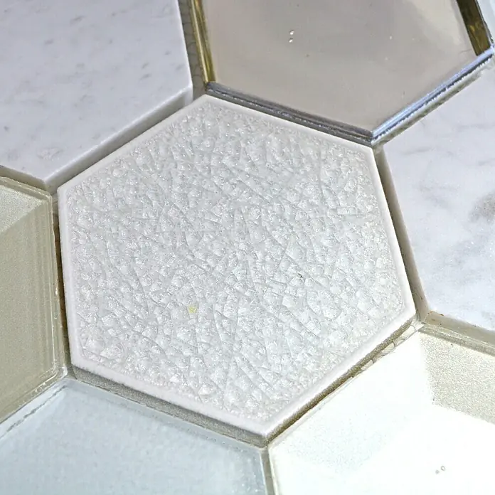 Mosaikfliese Hexagon HXN 66 - 26,5 x 30,5 cm, Weiß, Glänzend - Nahaufnahme von weißen, sechseckigen Fliesen mit einem feinen, rissartigen Muster, umgeben von andersfarbigen Fliesen.