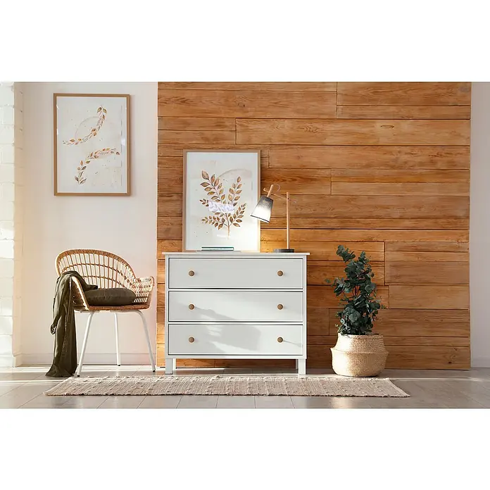 Nesu Pomo para muebles Haya - Ø x Al: 40 x 25 mm, Madera, Natural - Ambiente con una cómoda blanca de tres cajones, una lámpara y una planta de interior en una cesta de mimbre sobre una alfombra estampada.