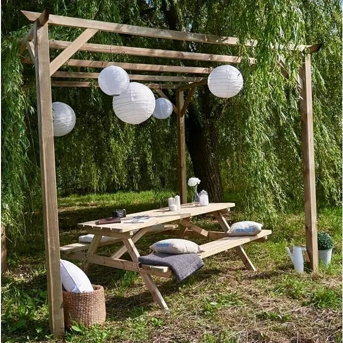 Cerland Pérgola estándar Patagonie - L x An: 300 x 300 cm, Natural - Un acogedor lugar de picnic bajo una pérgola de madera con farolillos de papel, una mesa con velas y cojines decorativos.