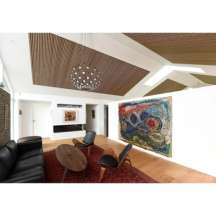 FibroTech Akustikpaneel Premium - Oiled Oak, 2.440 x 605 x 22 mm - Ein heller Wohnraum mit einem dunklen Ledersofa und einem Kunstwerk. Die Decke ist mit Holz verkleidet und eine kugelförmige Lampe hängt herab.