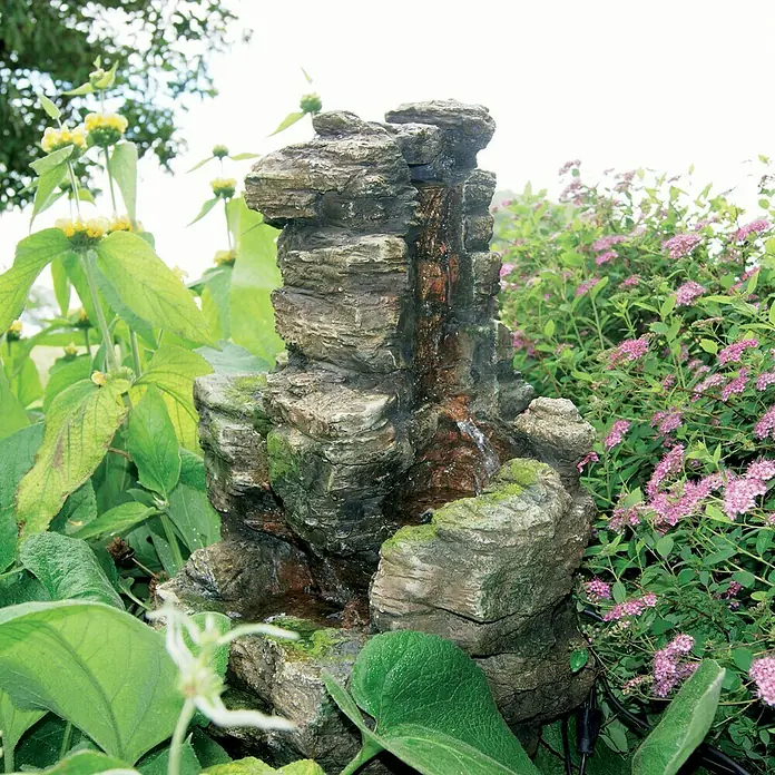 Ubbink AcquaArte Gartenbrunnen Chios - 47 x 32 x 58 cm, Kunststoff, Braun - Dekorative Gartenbrunnen mit mehrschichtiger Steinoptik, umgeben von üppiger Vegetation.