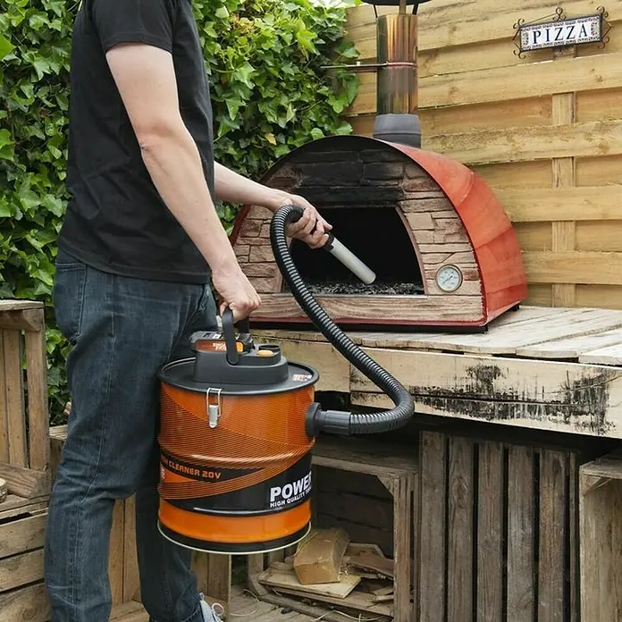 PowerPlus Aspirador de cenizas de batería POWD6020 - 20 V, Sin batería, Volumen de recipiente: 20 l - La aspiradora portátil con su cuerpo naranja se utiliza para limpiar un horno de pizza al aire libre.