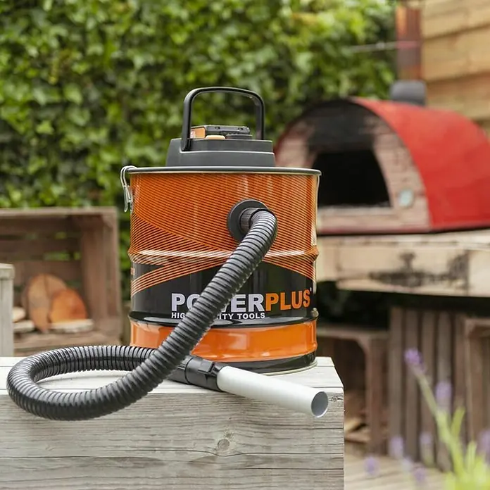 PowerPlus Aspirador de cenizas de batería POWD6020 - 20 V, Sin batería, Volumen de recipiente: 20 l - Aquí hay una foto de un aspirador de cenizas Powerplus que descansa sobre una mesa de madera al aire libre con un horno para pizzas al fondo.