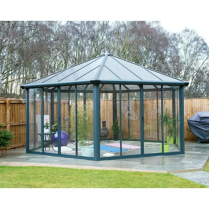Palram – Canopia Pérgola de jardín cerrado Garda - L x An x Al: 5,95 x 5,17 x 3,13 m, Aluminio, Gris - La imagen muestra un cenador con paredes de cristal y techo transparente, situado en el jardín sobre un patio.