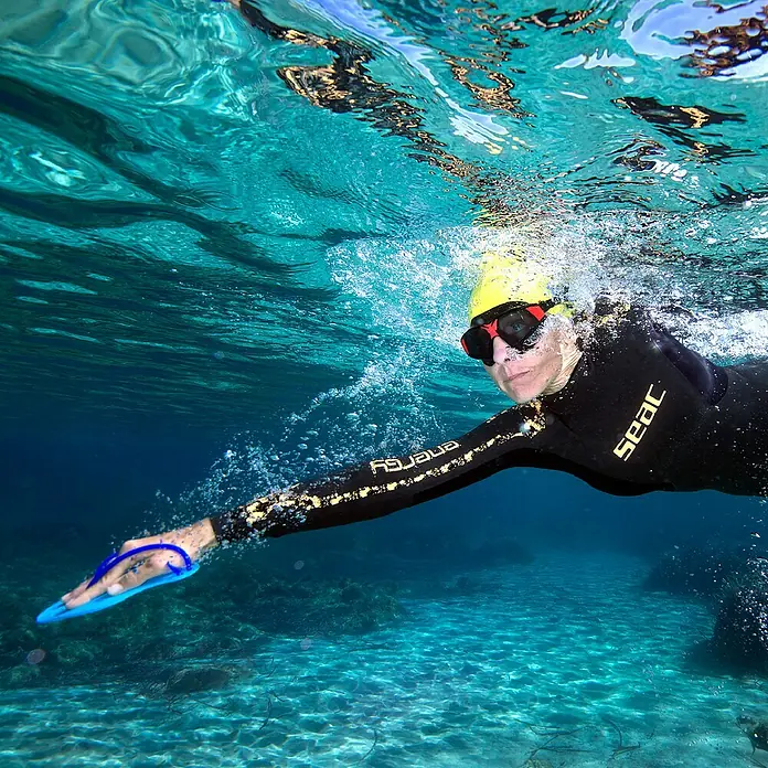 Seac Sub Palas de natación - M, Azul - Foto submarina de una nadadora con paletas de mano. La nadadora lleva un gorro de baño amarillo y gafas oscuras.