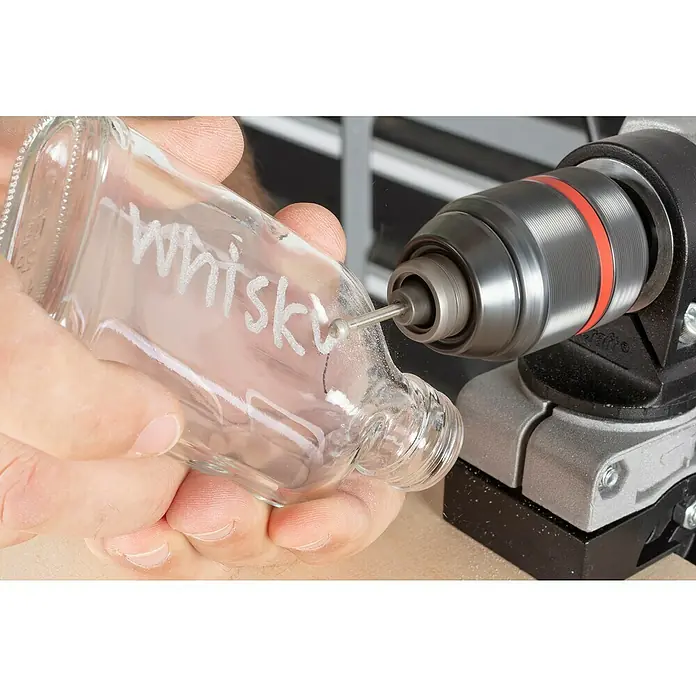 Wolfcraft Fresa de diamante - Diámetro: 3 mm - 5 mm, Diámetro vástago: 3 mm, 3 pzs. - Primer plano de una persona usando una herramienta de grabado en una botella de vidrio con la palabra "whisky" grabada.