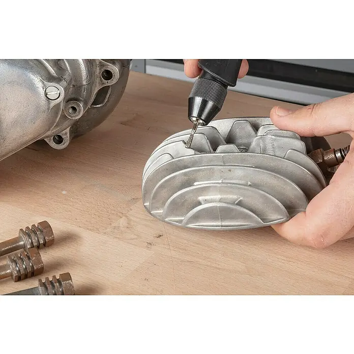 Wolfcraft Fresa de diamante - Diámetro: 4 mm - 5,5 mm, Diámetro vástago: 3 mm, 3 pzs. - Primer plano de alguien que utiliza una herramienta Dremel para trabajar una pieza de metal, con otras piezas sobre una mesa de madera.