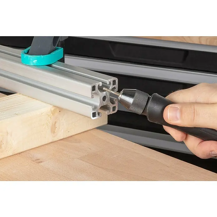 Wolfcraft Fresa de diamante - Diámetro: 4 mm - 5,5 mm, Diámetro vástago: 3 mm, 3 pzs. - Una mano está perforando un perfil de aluminio plateado, que está fijado con una abrazadera en una mesa de madera, utilizando un taladro de mano.