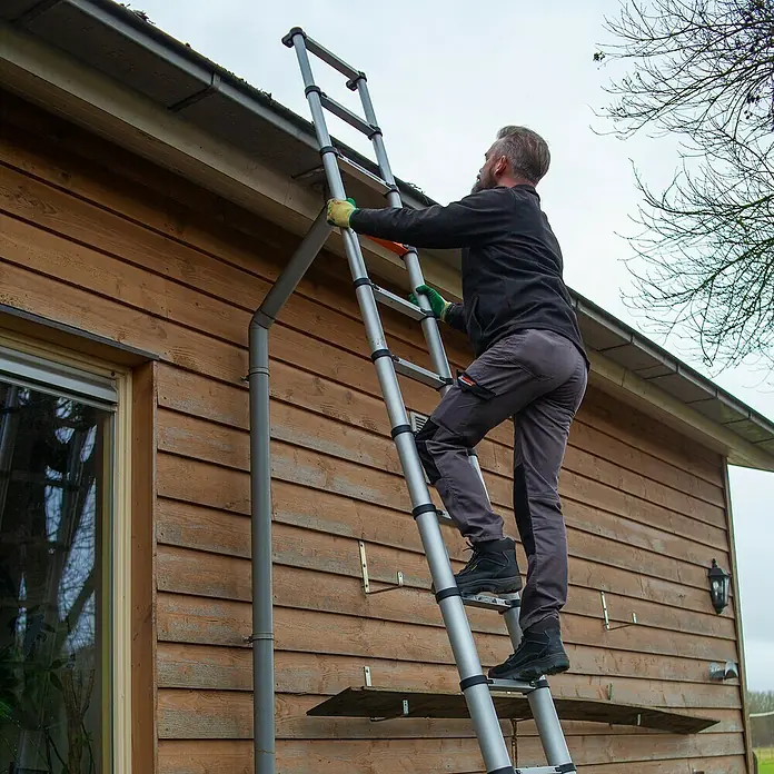 Batavia Teleskopleiter Professional - B x H: 88 x 9 cm, Anzahl Tritte: 12 Stk., Arbeitshöhe: 4,6 m - Eine Teleskopleiter wird von einem Mann benutzt, um an einem Gebäude zu arbeiten. Die Leiter ist ausziehbar und hat eine Plattform.