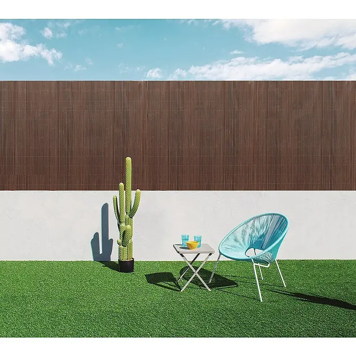 Nortene Sichtschutz LOP - Walnuss, L x H: 300 x 150 cm - Eine grüne Outdoor-Szene mit einem Kaktus, einem Tisch mit Geschirr und einem blauen Stuhl vor einem braunen Zaun.