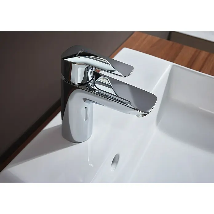 Hansgrohe MySport Waschtischarmatur L - Chrom, Glänzend - Ein moderner, verchromter Hansgrohe Waschtischmischer auf einem weißen Keramikwaschbecken mit Holzelementen im Hintergrund.