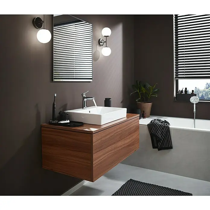 Hansgrohe Talis E Waschtischarmatur 110 - Chrom, Glänzend - Ein Badezimmerwaschbecken aus Holz mit einem eckigen, weißen Waschbeckenaufsatz und minimalistischen Armaturen unter einem Spiegel.