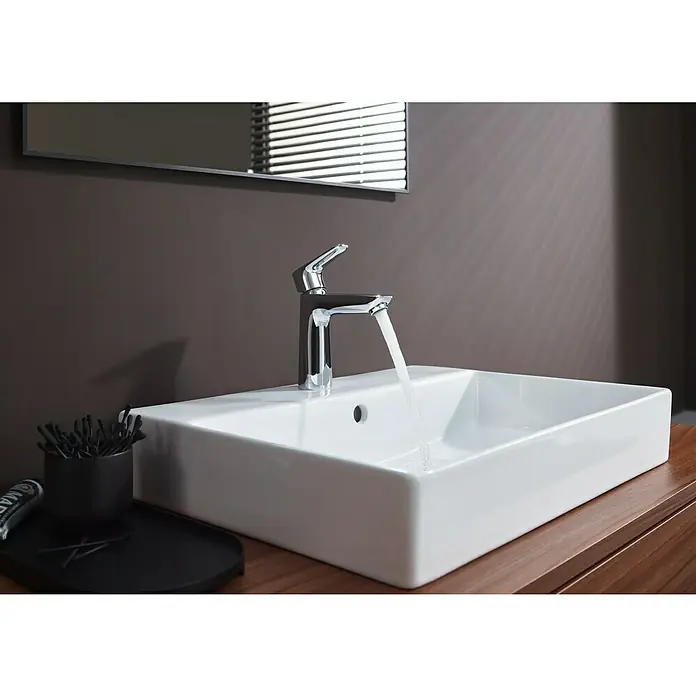 Hansgrohe Talis E Waschtischarmatur 110 - Chrom, Glänzend - Moderne Badezimmerarmatur mit fließendem Wasser in ein elegantes, rechteckiges Waschbecken, das auf einer Holzoberfläche steht.