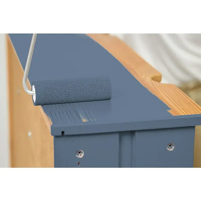 swingcolor Buntlack Acryl - Taubenblau, Glänzend, 2,5 l, Wasserbasiert - Nahaufnahme einer Person, die mit einer Farbwalze ein Holzmöbelstück mit blauer Farbe streicht.