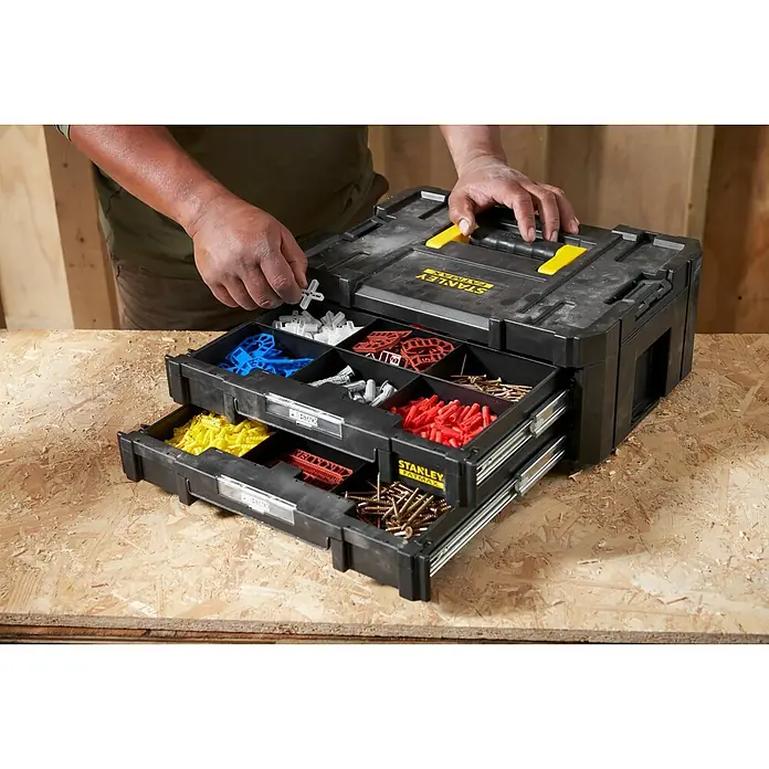 Stanley TSTAK Caja para herramientas con 2 cajones - 31,42 x 44 x 17,6 cm - Una caja de herramientas negra Stanley Fatmax con detalles amarillos y cajones llenos de tornillos y tacos, sobre una superficie de madera.