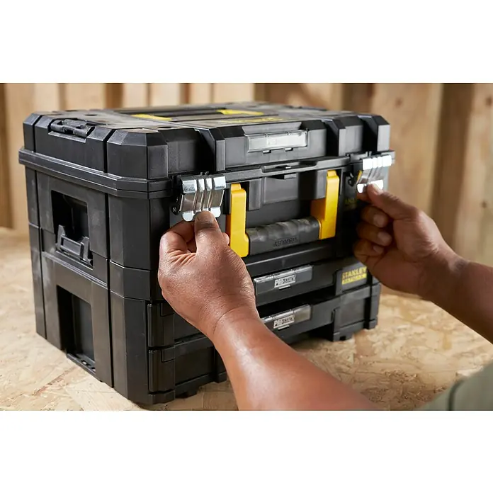 Stanley TSTAK Caja para herramientas grande con 2 cajones - 33,17 x 44 x 32,16 cm - Un sistema de almacenamiento Stanley Pro-Stack negro con detalles amarillos está siendo operado por dos manos.