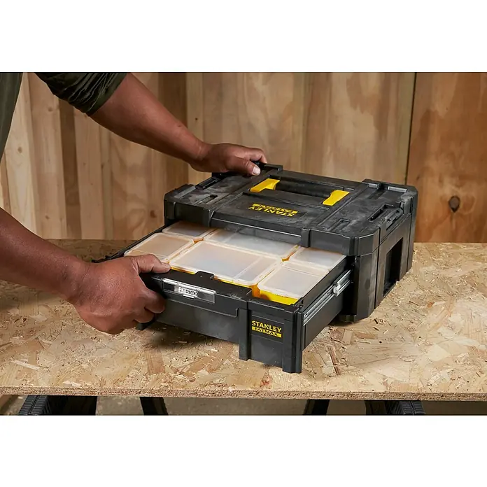 Stanley TSTAK Caja para herramientas Con cajones - 31,5 x 42,5 x 17,6 cm - Una persona abre una caja de herramientas negra Stanley Fatmax Pro-Stack con cajones sobre una mesa.