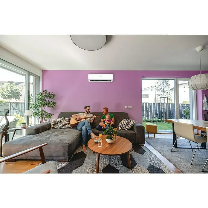 Bosch Aire acondicionado Inverter Climate 2000 - 2.600 W, 3.000 W, 16 m², Blanco - Un salón moderno con un aire acondicionado split en la pared morada, debajo del cual una familia está sentada en un sofá gris tocando la guitarra.