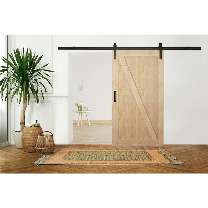 Puerta corredera de madera Riley - An x Al: 85 x 210 cm - Una puerta de estilo granero de madera clara con herrajes y manija corredizas negras. Una alfombra decorativa se encuentra frente a la puerta en el piso de parquet.
