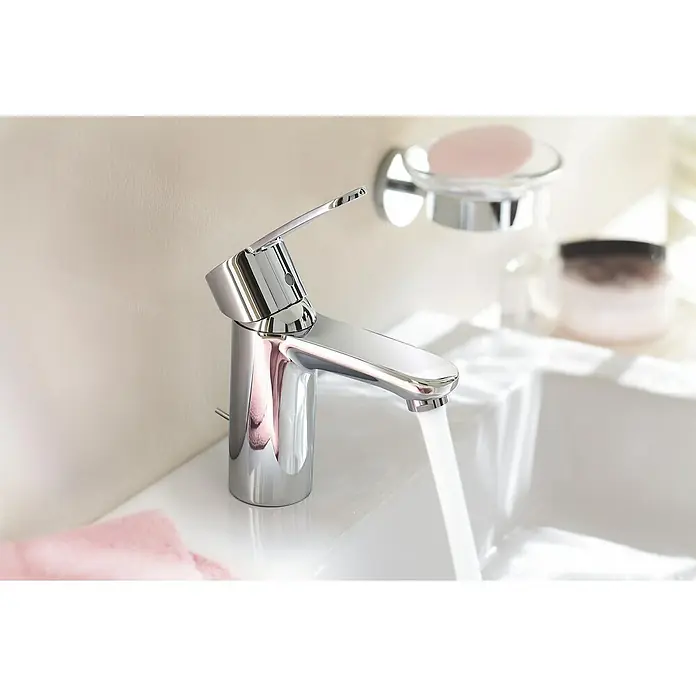 Grohe Eurostyle Cosmopolitan Waschtischarmatur - Chrom, Glänzend - Nahaufnahme eines glänzenden Wasserhahns mit fließendem Wasser in einem modernen Badezimmer, mit Seifenschale und Kosmetikprodukten im Hintergrund.