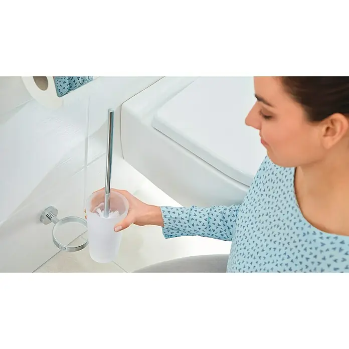 Tesa Smooz Conjunto de escobilla - Vidrio, Cromo - Una mujer sostiene un cepillo de baño con soporte en un baño que emana un ambiente limpio y moderno.