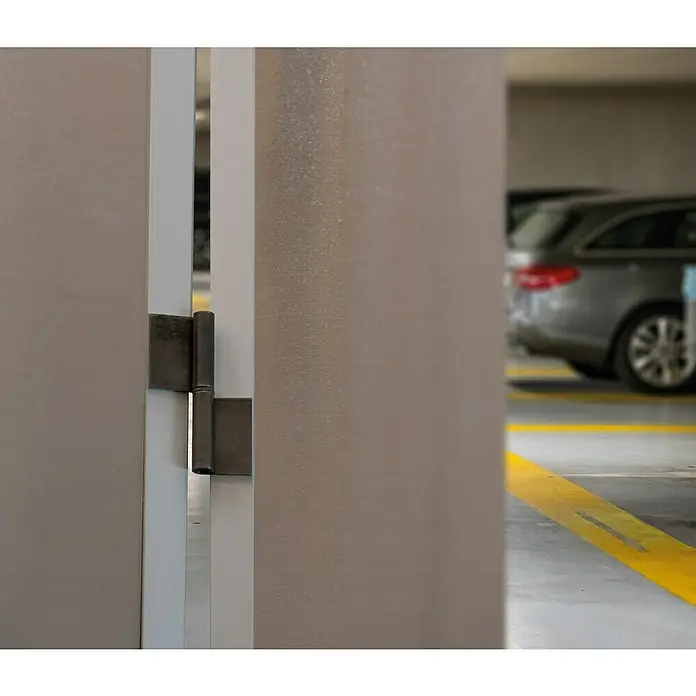 Pernio bisagra 1P - L x An: 80 x 10 mm, Izquierda - Primer plano de una bisagra de puerta con un garaje de estacionamiento al fondo. La bisagra tiene un diseño robusto y funcional.