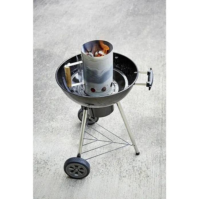 Grillstar Anzündkamin - Ø x H: 19 x 27 cm - Ein Holzkohlegrill mit einem Anzündkamin, in dem die Kohlen bereits glühen. Der Grill steht auf einer betonierten Fläche im Freien.