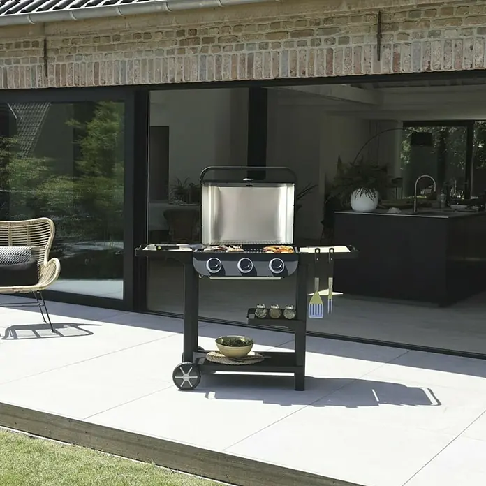 Barbacoa de gas Flavo 60 - Número de quemadores: 3 ud. - Una parrilla de gas negra con detalles de acero inoxidable en un patio listo para asados al aire libre.
