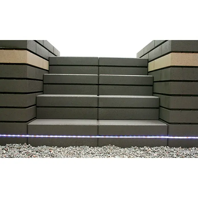 Christoph Mauerstein C-Line - Grau, 50 x 25 x 10 cm, Beton - Betonstufen mit LED-Beleuchtung, umgeben von grauen Betonblöcken und Kies. Die Stufen bieten einen modernen und sicheren Zugang im Außenbereich.