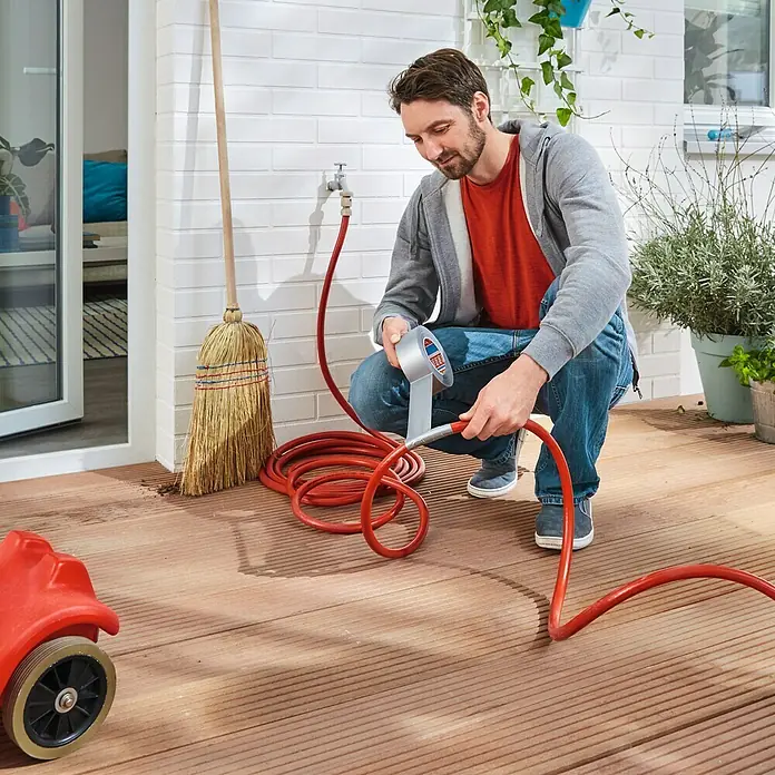 Tesa Extra Power Folienband Universal - Silber, 50 m x 50 mm - Ein Mann repariert einen roten Gartenschlauch mit Tesa-Band auf einer Terrasse.