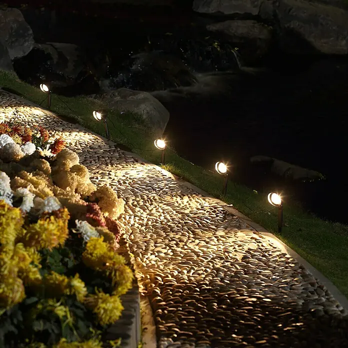 Starlux LED-Gartenspot-Set Bari - 4 W, IP44, Schwarz - Gartenwegbeleuchtung mit warmem Licht entlang eines Kieswegs, der mit bunten Blumen geschmückt ist.