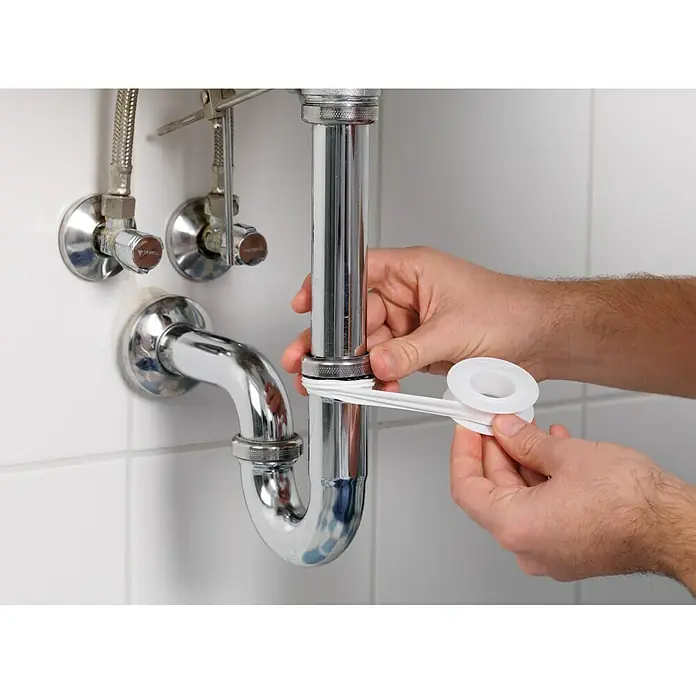 Tesa Cinta Stop Water - Blanco, 12 m x 12 mm - Un fontanero está aplicando cinta de PTFE a un tubo de desagüe del lavabo para sellar la conexión y evitar fugas.