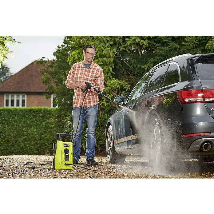 Ryobi Hochdruckreiniger RY110PWA - 1.400 W - Ein Mann benutzt einen RYOBI Hochdruckreiniger, um ein Auto zu waschen. Der Reiniger steht neben ihm und ist an eine Stromquelle angeschlossen.