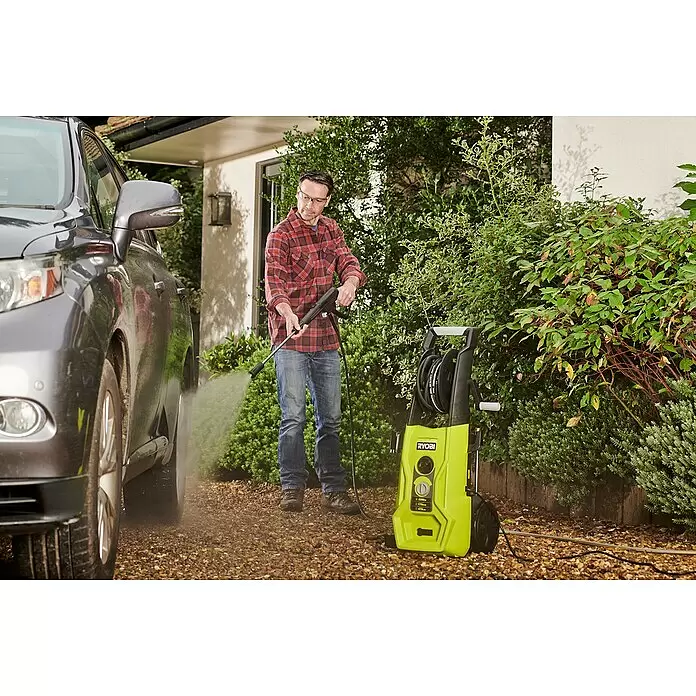 Ryobi Hochdruckreiniger RY170PWA - 2.500 W - Ein Mann nutzt einen lindgrün-schwarzen Ryobi Hochdruckreiniger, um ein graues Auto in einer Einfahrt zu reinigen.