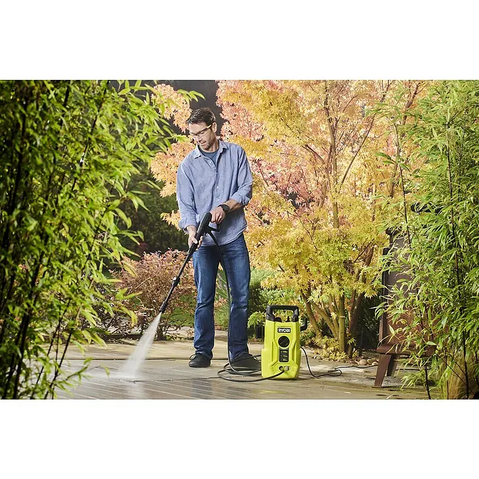 Ryobi Hochdruckreiniger RY110PWA - 1.400 W - Ein Mann benutzt einen Ryobi-Hochdruckreiniger, um eine Terrasse zu säubern, mit herbstlichen Bäumen im Hintergrund.